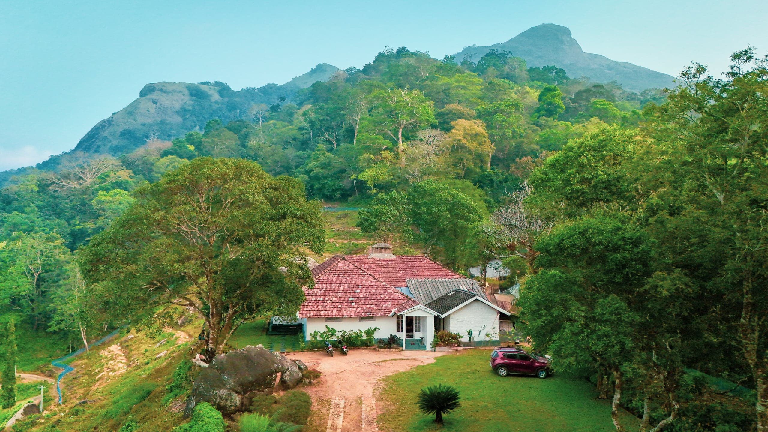 Aerial view of the 1930s planter's bungalow set in its plantation estate with hills beyond at Heyday Planter's Portico, near Thenmala, Kerala