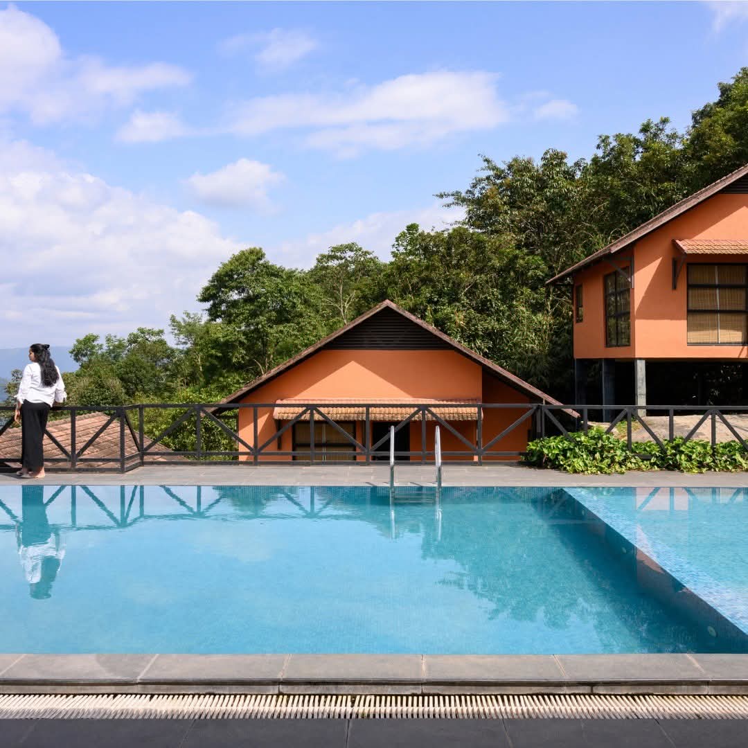 Infinity pool and terracotta cottages under a blue sky at Heyday Thazhvaram, Panchalimedu, Idukki, Kerala